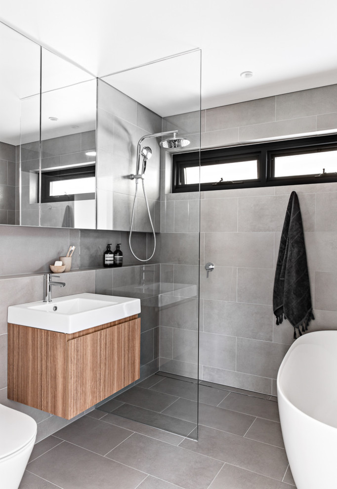 Idéer för små funkis en-suite badrum, med bruna skåp, ett fristående badkar, våtrum, en toalettstol med separat cisternkåpa, grå kakel, porslinskakel, grå väggar, klinkergolv i porslin, ett väggmonterat handfat, grått golv och med dusch som är öppen