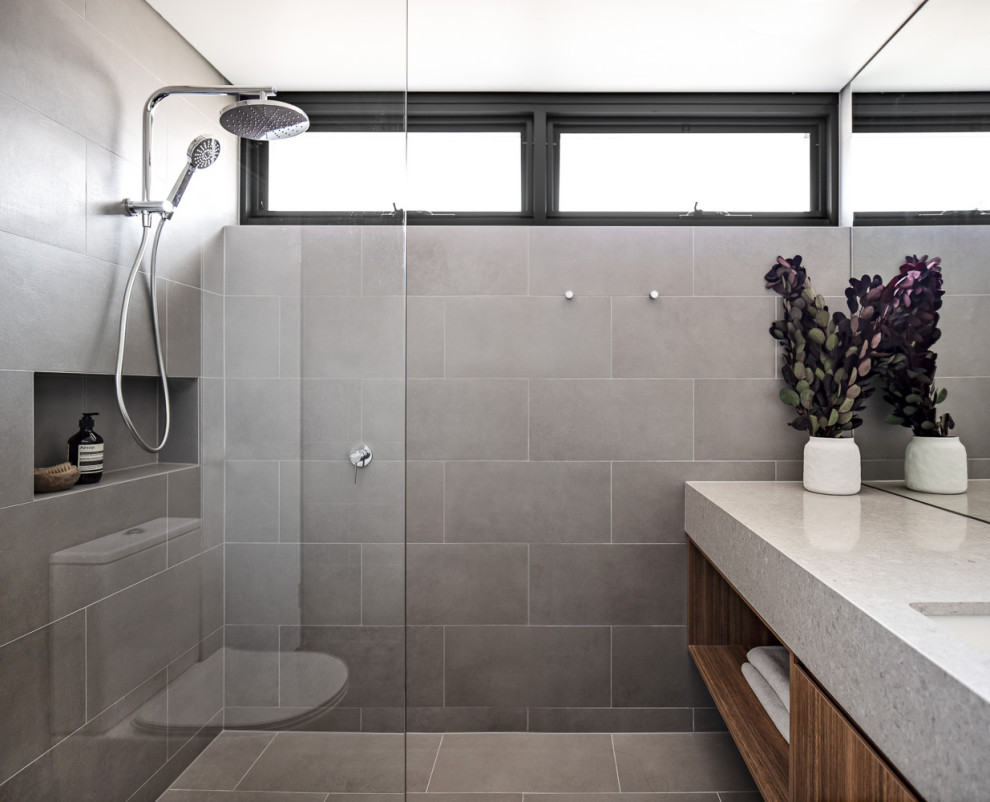 Idée de décoration pour une petite salle de bain principale design avec des portes de placard marrons, un espace douche bain, WC à poser, un carrelage gris, des carreaux de porcelaine, un mur gris, un sol en carrelage de porcelaine, un lavabo encastré, un plan de toilette en quartz modifié, un sol gris, aucune cabine, un plan de toilette gris, meuble simple vasque et meuble-lavabo suspendu.