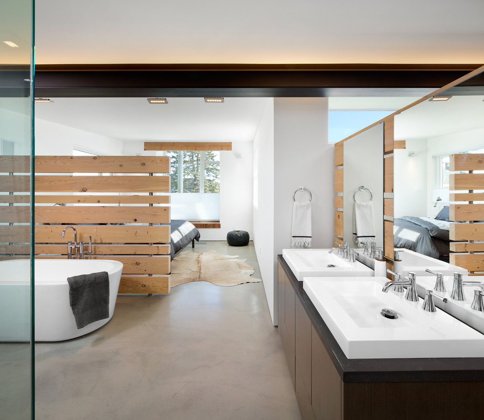 バンクーバーにあるコンテンポラリースタイルのおしゃれな浴室 (ベッセル式洗面器、フラットパネル扉のキャビネット、濃色木目調キャビネット、置き型浴槽、白い壁、コンクリートの床) の写真