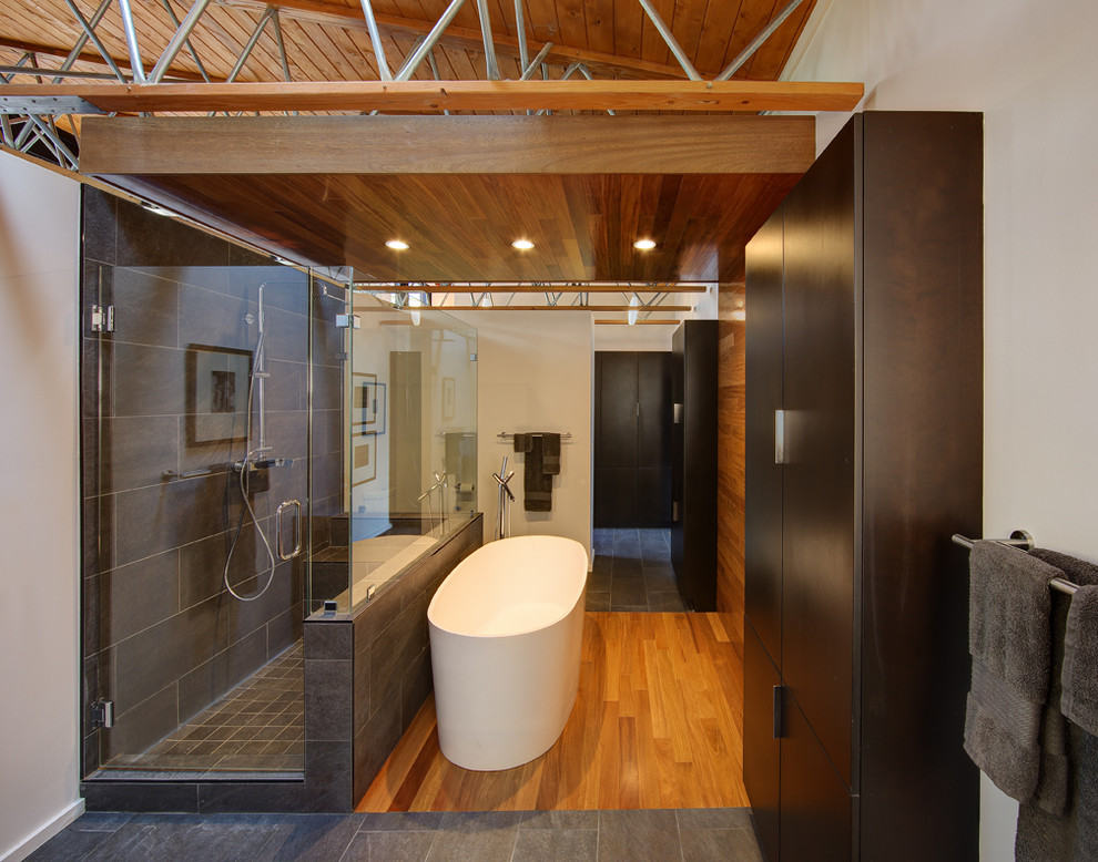 Medium sized contemporary ensuite bathroom in Milwaukee with a freestanding bath, flat-panel cabinets, dark wood cabinets, white walls, medium hardwood flooring, a hinged door, a corner shower and brown floors.