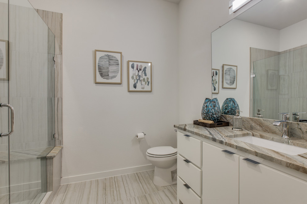 Inspiration for a mid-sized contemporary 3/4 brown tile and porcelain tile porcelain tile and gray floor alcove shower remodel in Dallas with flat-panel cabinets, white cabinets, granite countertops, beige countertops, a two-piece toilet, white walls, an undermount sink and a hinged shower door