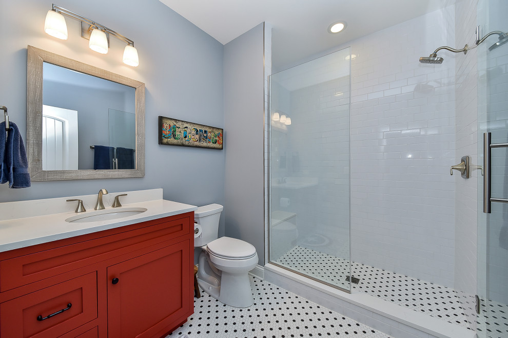 Klassisk inredning av ett mellanstort vit vitt badrum för barn, med luckor med profilerade fronter, röda skåp, en dusch i en alkov, en toalettstol med separat cisternkåpa, vit kakel, tunnelbanekakel, grå väggar, klinkergolv i keramik, ett undermonterad handfat, bänkskiva i kvarts, flerfärgat golv och dusch med gångjärnsdörr