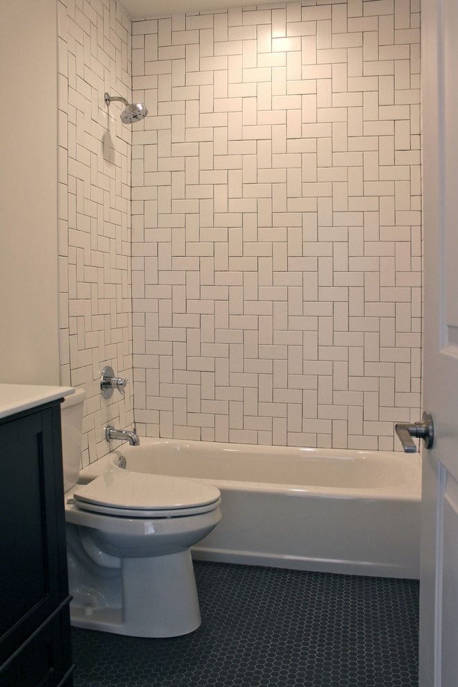 Bild på ett litet industriellt badrum, med ett undermonterad handfat, luckor med infälld panel, svarta skåp, bänkskiva i akrylsten, ett badkar i en alkov, en dusch/badkar-kombination, en toalettstol med separat cisternkåpa, vit kakel, keramikplattor, vita väggar och klinkergolv i porslin