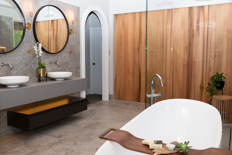 На фото: ванная комната в современном стиле с отдельно стоящей ванной, серой плиткой, серыми стенами, настольной раковиной, серым полом, серой столешницей, тумбой под две раковины и подвесной тумбой с
