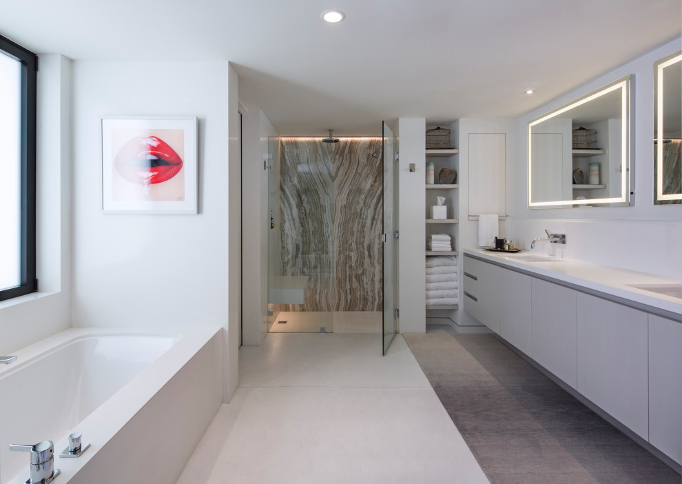Modern inredning av ett vit vitt badrum, med släta luckor, grå skåp, ett undermonterat badkar, grå kakel, vita väggar, ett undermonterad handfat och grått golv