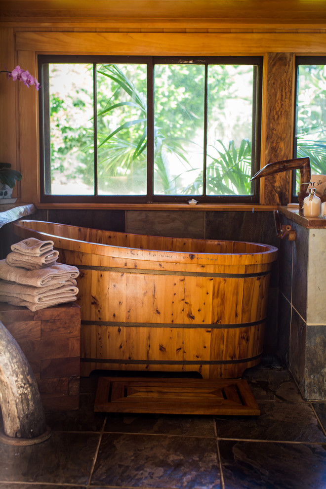 Foto de cuarto de baño tropical grande con bañera japonesa, ducha abierta, baldosas y/o azulejos grises, baldosas y/o azulejos de piedra, paredes grises, suelo de pizarra y encimera de madera
