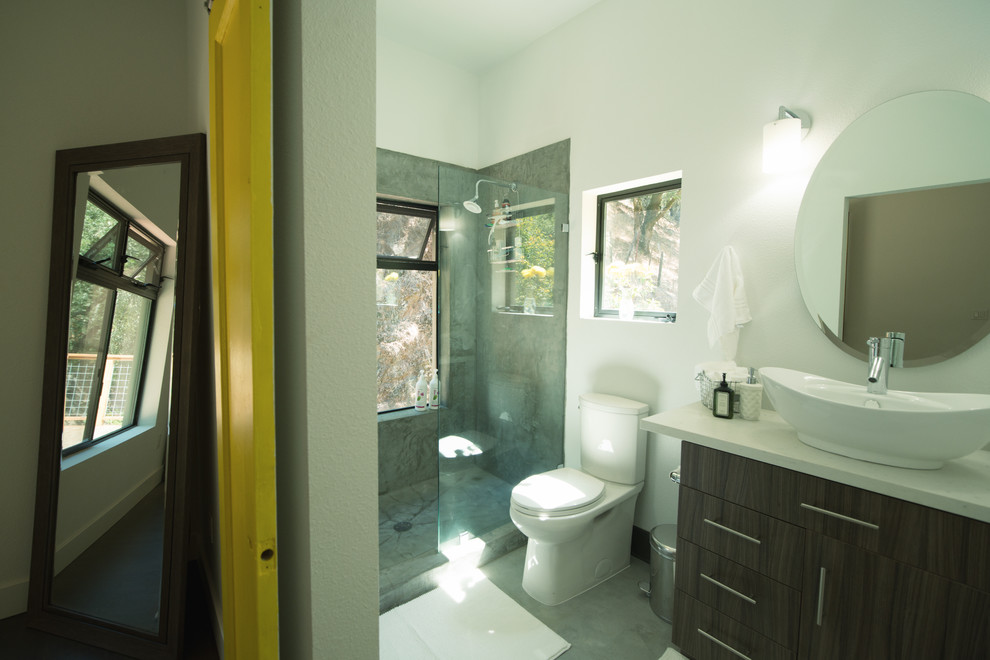Cette photo montre une petite salle de bain principale moderne en bois foncé avec une vasque, un placard à porte plane, un plan de toilette en surface solide, une douche à l'italienne, WC à poser, un mur blanc et sol en béton ciré.