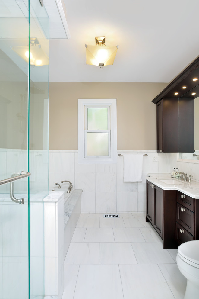 Cette photo montre une douche en alcôve chic en bois foncé avec un placard avec porte à panneau encastré, une baignoire posée, WC à poser, un mur marron, un sol en marbre, un lavabo encastré et un plan de toilette en marbre.