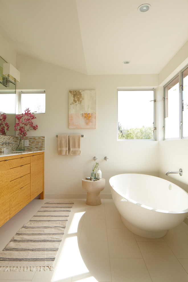 На фото: ванная комната в современном стиле с плоскими фасадами, фасадами цвета дерева среднего тона, отдельно стоящей ванной, бежевой плиткой и фартуком с
