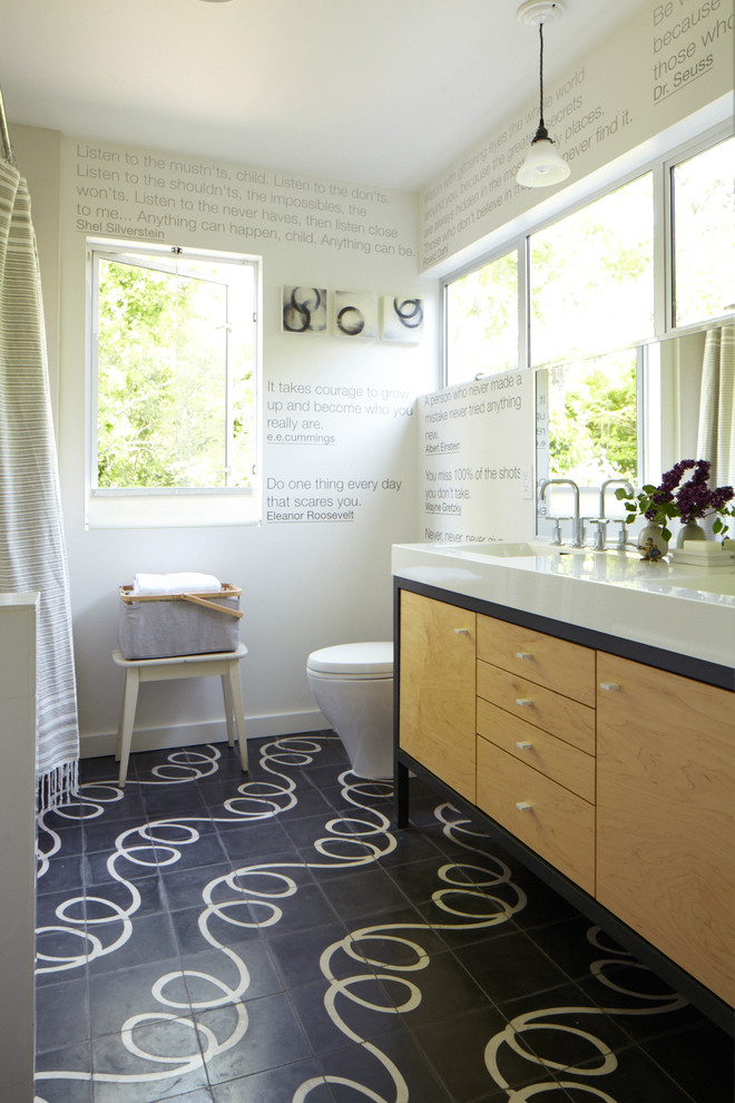 Imagen de cuarto de baño actual con lavabo integrado, armarios con paneles lisos, puertas de armario de madera clara, baldosas y/o azulejos negros y encimeras blancas