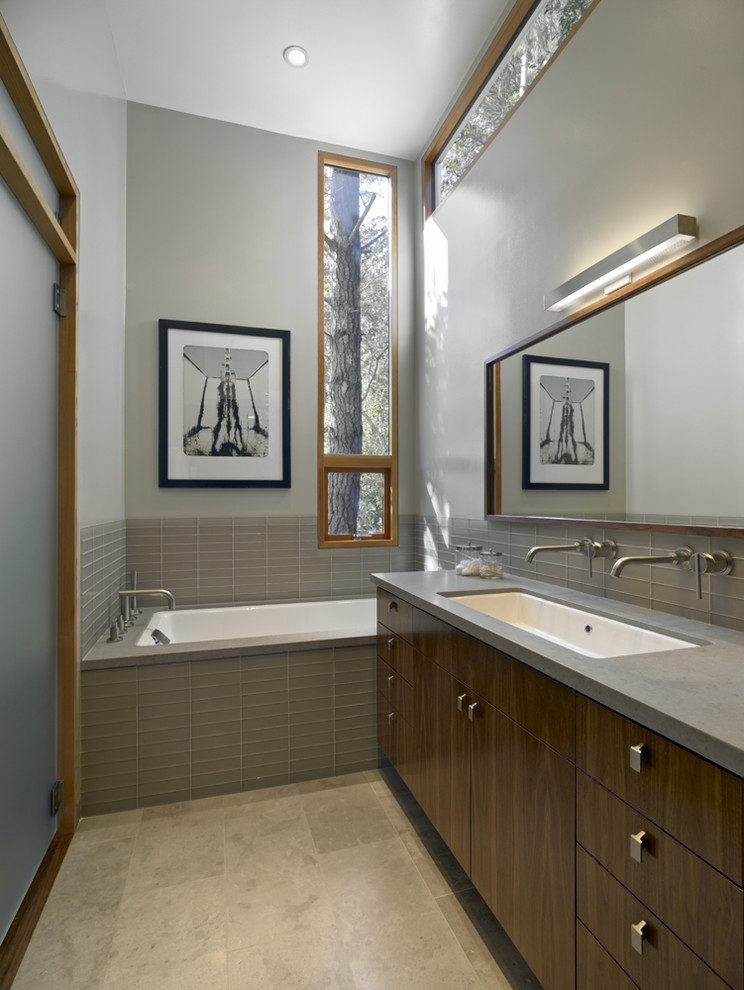 Идея дизайна: главная ванная комната в стиле модернизм с раковиной с несколькими смесителями, плоскими фасадами, темными деревянными фасадами, полновстраиваемой ванной, серой плиткой, стеклянной плиткой, серыми стенами и столешницей из искусственного кварца