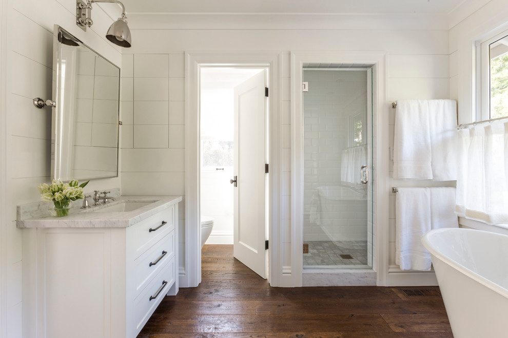 Inredning av ett lantligt stort en-suite badrum, med ett undermonterad handfat, vita skåp, en dusch i en alkov, vit kakel, vita väggar, mörkt trägolv, skåp i shakerstil, ett fristående badkar, tunnelbanekakel och brunt golv