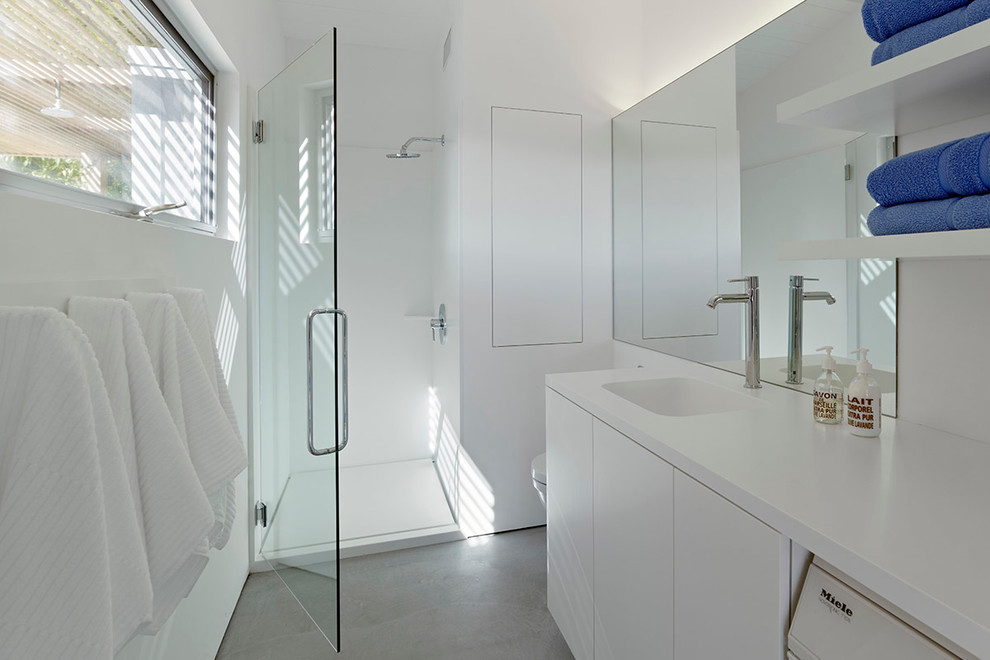 Photo of a medium sized modern bathroom in San Francisco with an alcove shower, an integrated sink, flat-panel cabinets, white cabinets, solid surface worktops, a wall mounted toilet, white walls, concrete flooring and white worktops.