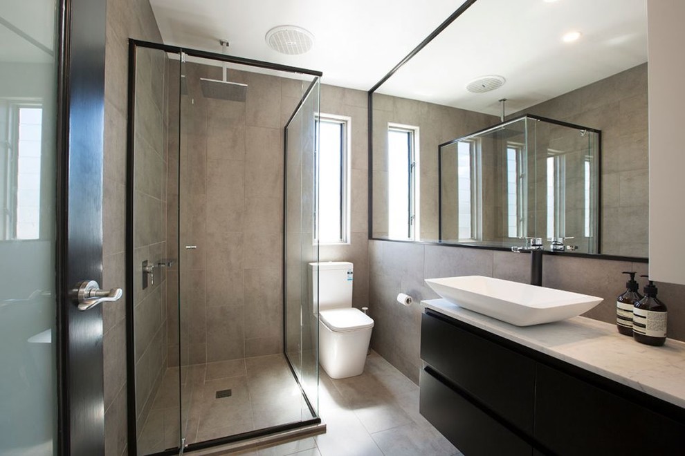 This is an example of a medium sized modern ensuite bathroom in Melbourne with shaker cabinets, black cabinets, a corner shower, a one-piece toilet, grey tiles, porcelain tiles, grey walls, porcelain flooring, a vessel sink, marble worktops, grey floors and a hinged door.