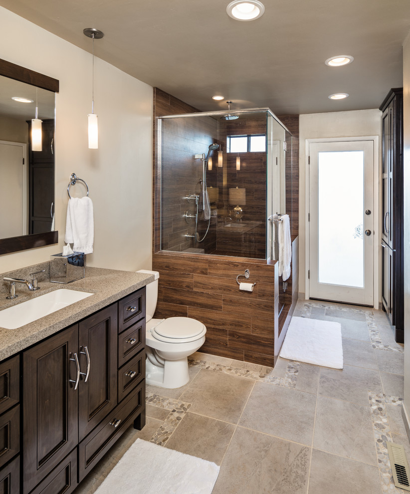 Design ideas for a medium sized contemporary ensuite bathroom in San Luis Obispo with glass-front cabinets, dark wood cabinets, a corner shower, a two-piece toilet, brown tiles, ceramic tiles, beige walls, travertine flooring, a built-in sink, granite worktops, beige floors, a hinged door and beige worktops.