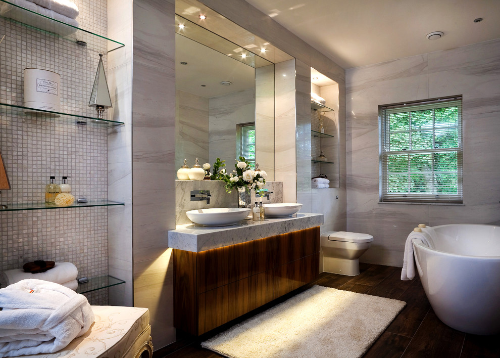 На фото: главная ванная комната среднего размера в современном стиле с настольной раковиной, плоскими фасадами, темными деревянными фасадами, отдельно стоящей ванной, унитазом-моноблоком и серыми стенами