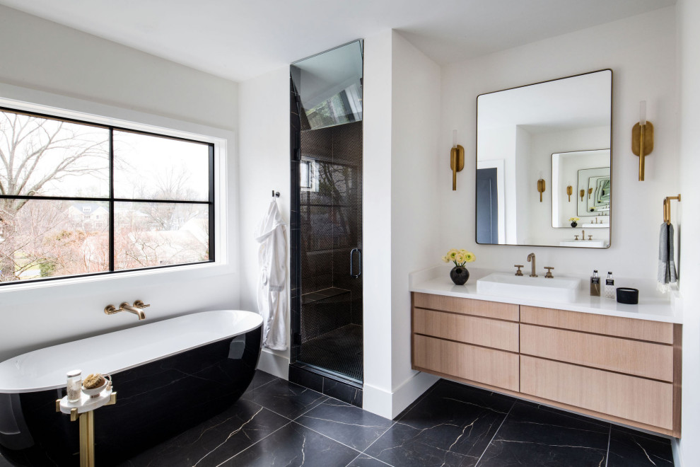 Bild på ett funkis vit vitt badrum, med släta luckor, skåp i ljust trä, ett fristående badkar, svart kakel, vita väggar, ett fristående handfat och svart golv