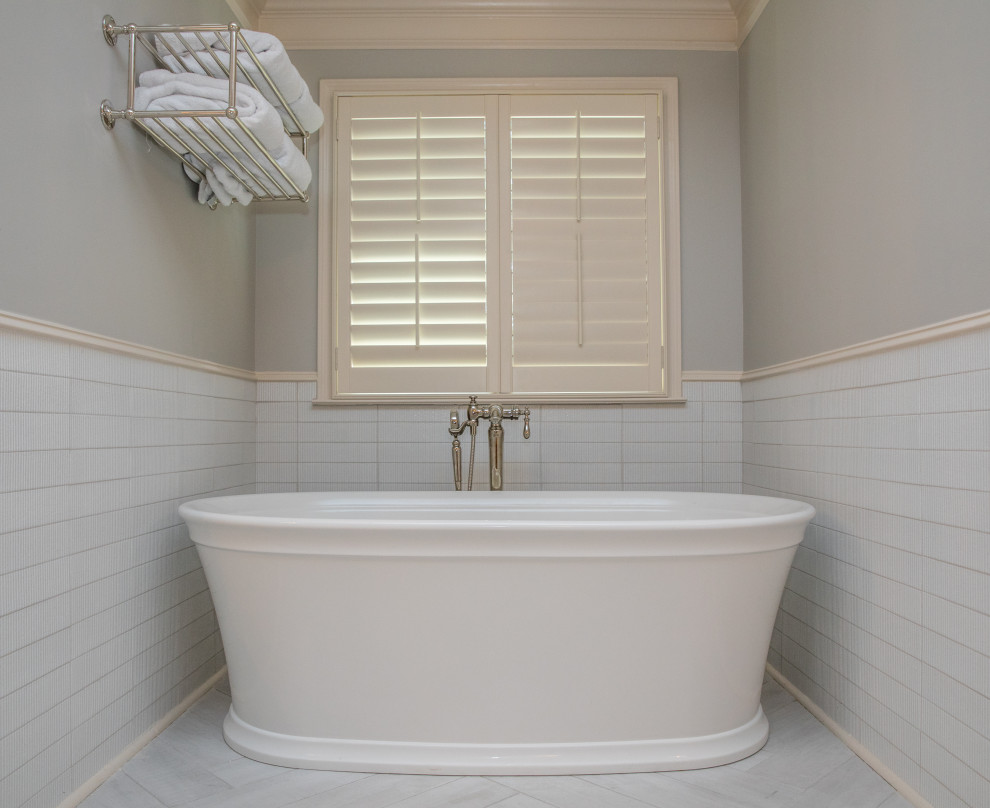 Свежая идея для дизайна: большая главная ванная комната в стиле фьюжн с плоскими фасадами, белыми фасадами, отдельно стоящей ванной, открытым душем, унитазом-моноблоком, белой плиткой, керамической плиткой, серыми стенами, полом из керамогранита, врезной раковиной, столешницей из искусственного кварца, серым полом, душем с распашными дверями, белой столешницей, сиденьем для душа, тумбой под две раковины, встроенной тумбой и панелями на стенах - отличное фото интерьера