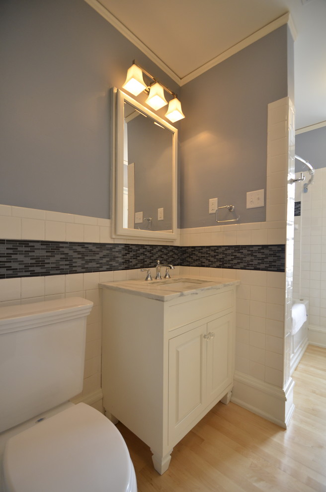 Immagine di una stanza da bagno chic con lavabo sottopiano, ante bianche, top in marmo, vasca ad alcova, WC monopezzo, pareti blu, parquet chiaro e ante con bugna sagomata