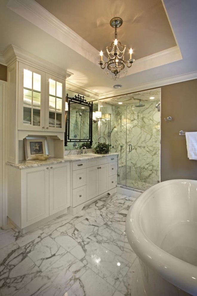 Inredning av ett stort en-suite badrum, med ett nedsänkt handfat, luckor med glaspanel, vita skåp, marmorbänkskiva, ett badkar med tassar, en hörndusch, en toalettstol med separat cisternkåpa, flerfärgad kakel, cementkakel, beige väggar och mellanmörkt trägolv