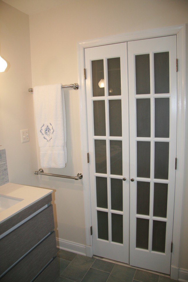 Modern inredning av ett litet en-suite badrum, med ett integrerad handfat, möbel-liknande, grå skåp, bänkskiva i akrylsten, en hörndusch, en toalettstol med hel cisternkåpa, blå kakel, mosaik, beige väggar och klinkergolv i keramik