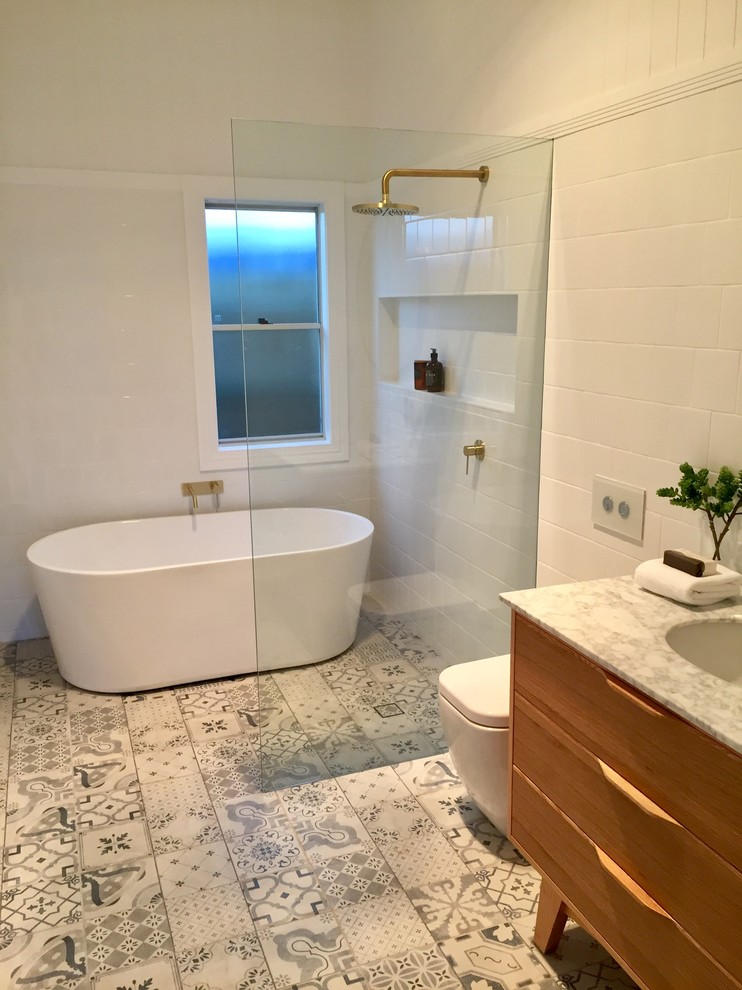 Стильный дизайн: ванная комната среднего размера в стиле модернизм с фасадами островного типа, светлыми деревянными фасадами, отдельно стоящей ванной, открытым душем, унитазом-моноблоком, белой плиткой, керамической плиткой, белыми стенами, полом из ламината, душевой кабиной, врезной раковиной, мраморной столешницей, разноцветным полом, открытым душем и белой столешницей - последний тренд