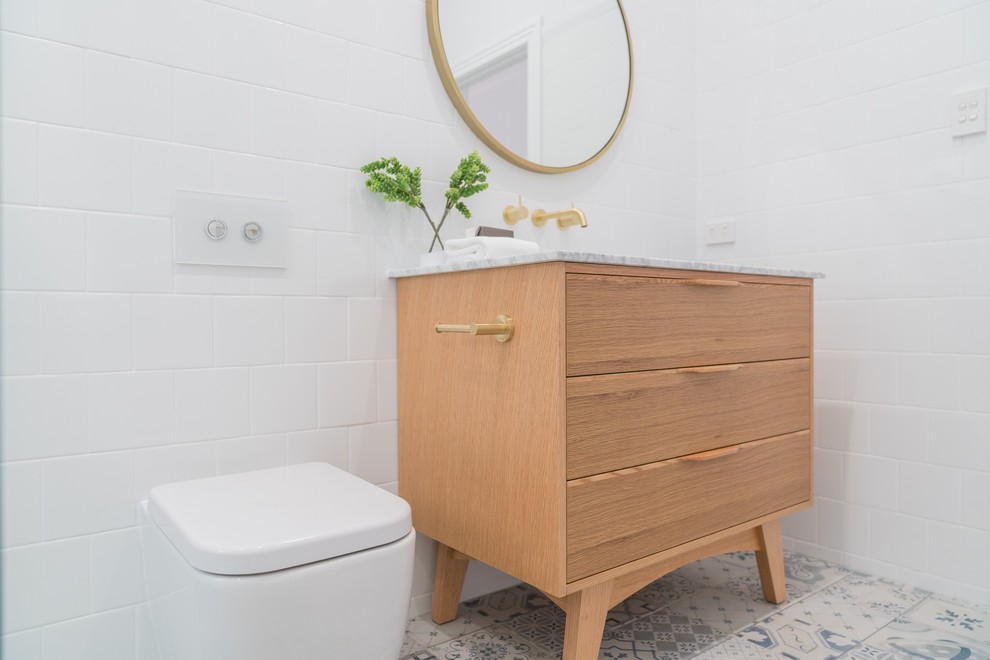 На фото: ванная комната среднего размера в стиле модернизм с фасадами островного типа, светлыми деревянными фасадами, отдельно стоящей ванной, открытым душем, унитазом-моноблоком, белой плиткой, керамической плиткой, белыми стенами, полом из ламината, душевой кабиной, врезной раковиной, мраморной столешницей, разноцветным полом, открытым душем и белой столешницей