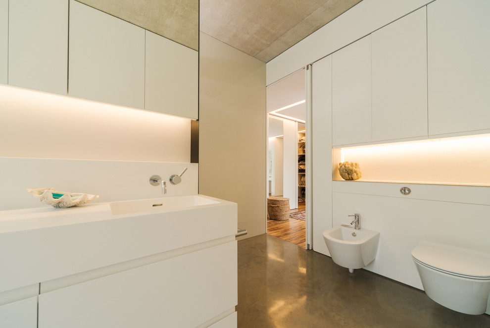 Immagine di una grande stanza da bagno per bambini design con ante lisce, ante bianche, doccia aperta, WC sospeso, lastra di vetro, pavimento in cemento, lavabo da incasso e top in vetro