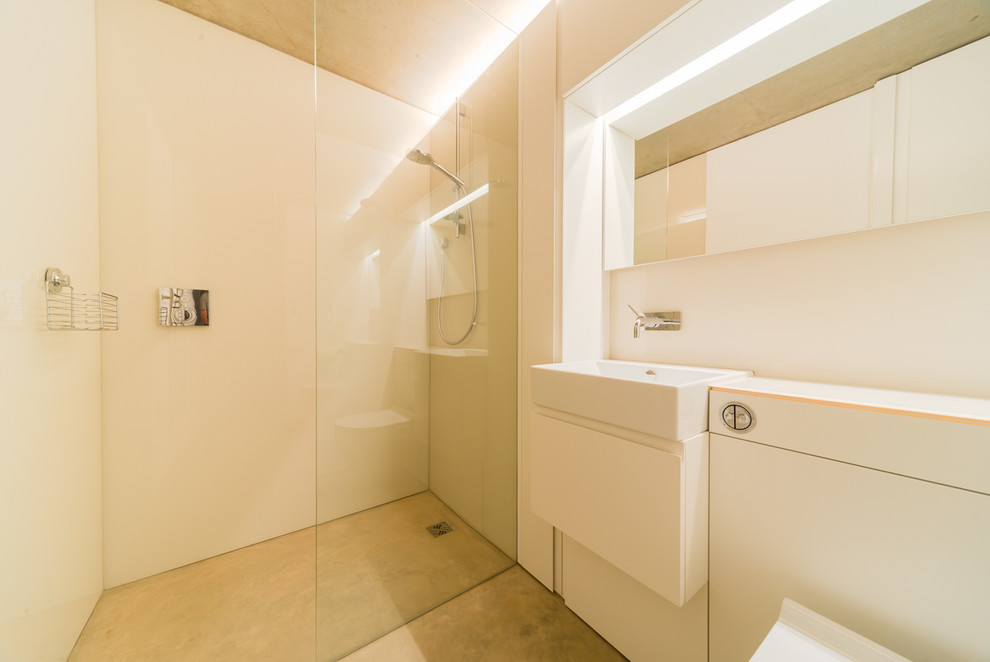 Exemple d'une salle de bain principale tendance de taille moyenne avec un placard à porte plane, des portes de placard blanches, une douche ouverte, WC suspendus, des plaques de verre, sol en béton ciré, un lavabo posé et un plan de toilette en verre.