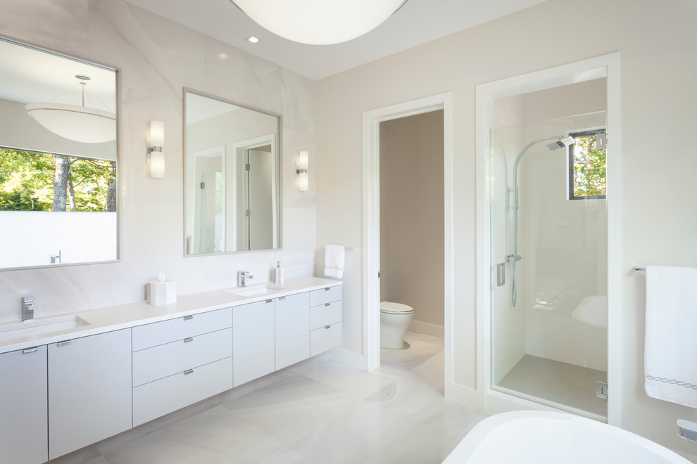 Inredning av ett skandinaviskt stort vit vitt en-suite badrum, med släta luckor, vita skåp, ett fristående badkar, en dusch i en alkov, beige väggar, marmorgolv, ett undermonterad handfat, bänkskiva i akrylsten, vitt golv och dusch med gångjärnsdörr