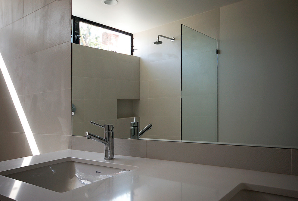 Modern inredning av ett stort badrum med dusch, med ett undermonterad handfat, bänkskiva i kvarts, en öppen dusch, vit kakel, porslinskakel, släta luckor, grå skåp, vita väggar och klinkergolv i porslin