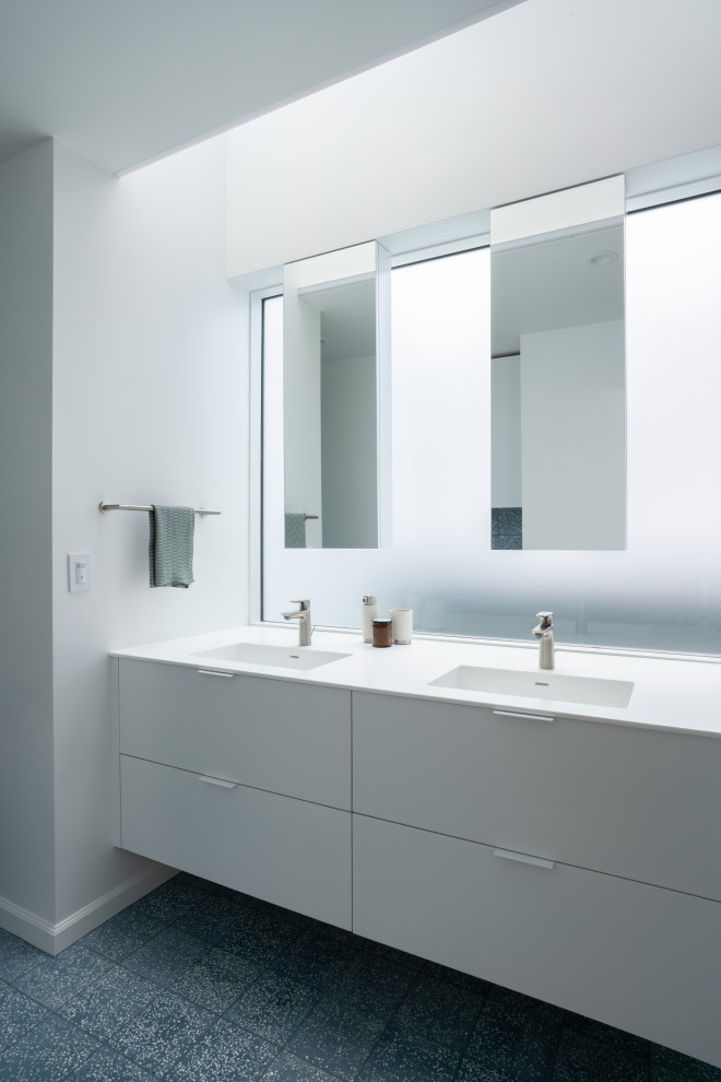 Exempel på ett mellanstort modernt vit vitt badrum för barn, med släta luckor, vita skåp, ett badkar i en alkov, en dusch/badkar-kombination, en vägghängd toalettstol, blå kakel, cementkakel, vita väggar, cementgolv, ett integrerad handfat, bänkskiva i akrylsten och blått golv