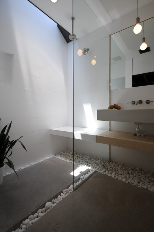 Inredning av ett modernt litet badrum med dusch, med ett avlångt handfat, öppna hyllor, skåp i ljust trä, bänkskiva i betong, en kantlös dusch, vit kakel, vita väggar och betonggolv