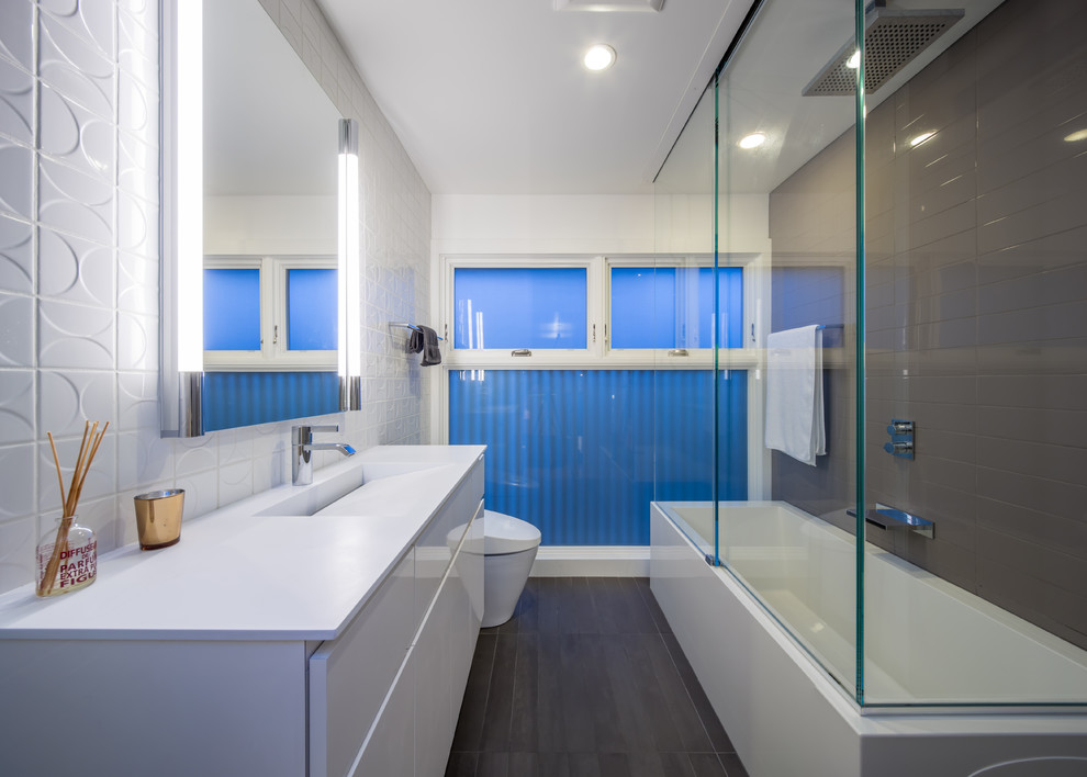 Idées déco pour une salle de bain moderne avec un lavabo intégré, un placard à porte plane, des portes de placard blanches, un carrelage gris et un plan de toilette blanc.