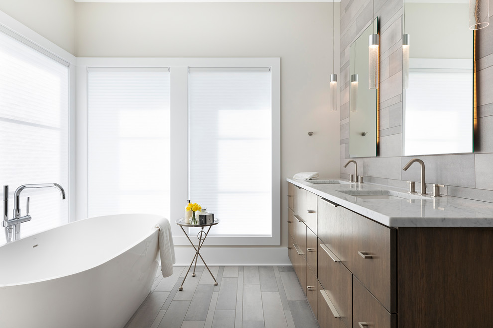 Стильный дизайн: главная ванная комната в современном стиле с плоскими фасадами, фасадами цвета дерева среднего тона, отдельно стоящей ванной, серой плиткой, белыми стенами, врезной раковиной, серым полом и белой столешницей - последний тренд