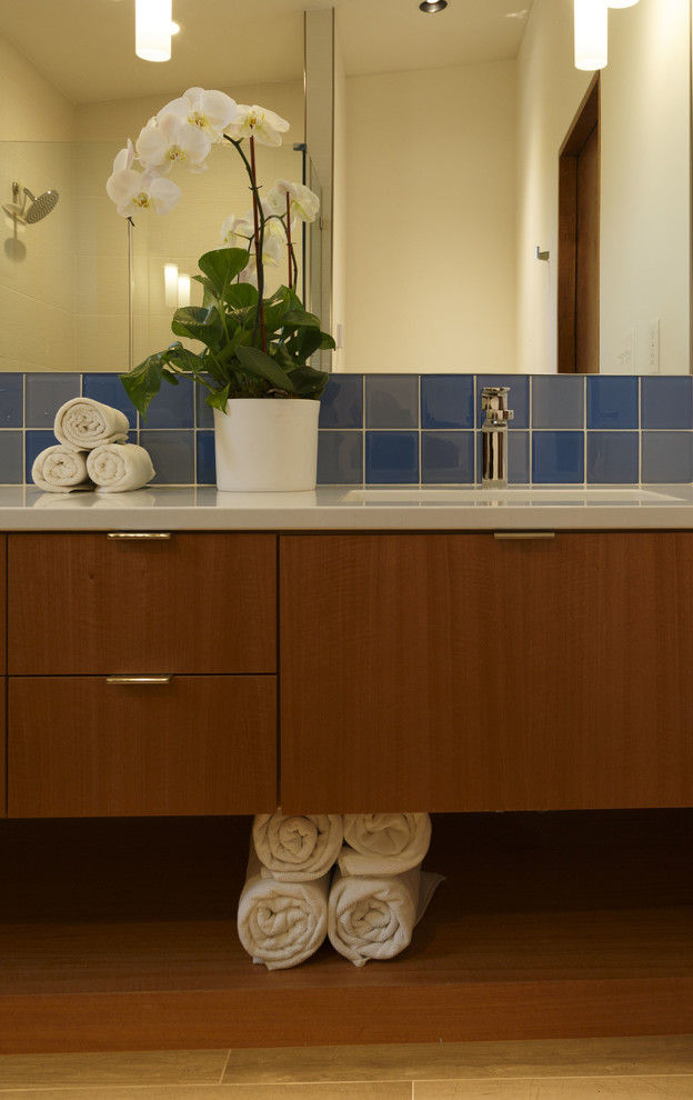 Пример оригинального дизайна: маленькая главная ванная комната в стиле модернизм с плоскими фасадами, фасадами цвета дерева среднего тона, раздельным унитазом, синей плиткой, белыми стенами, паркетным полом среднего тона, врезной раковиной и столешницей из искусственного кварца для на участке и в саду