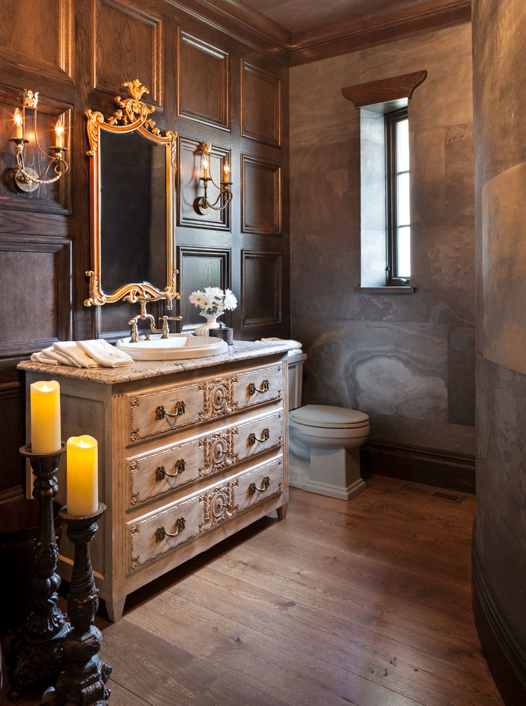 Klassisk inredning av ett badrum med dusch, med beige skåp, marmorbänkskiva, brun kakel, stenkakel, mellanmörkt trägolv, ett nedsänkt handfat, en toalettstol med separat cisternkåpa och luckor med upphöjd panel