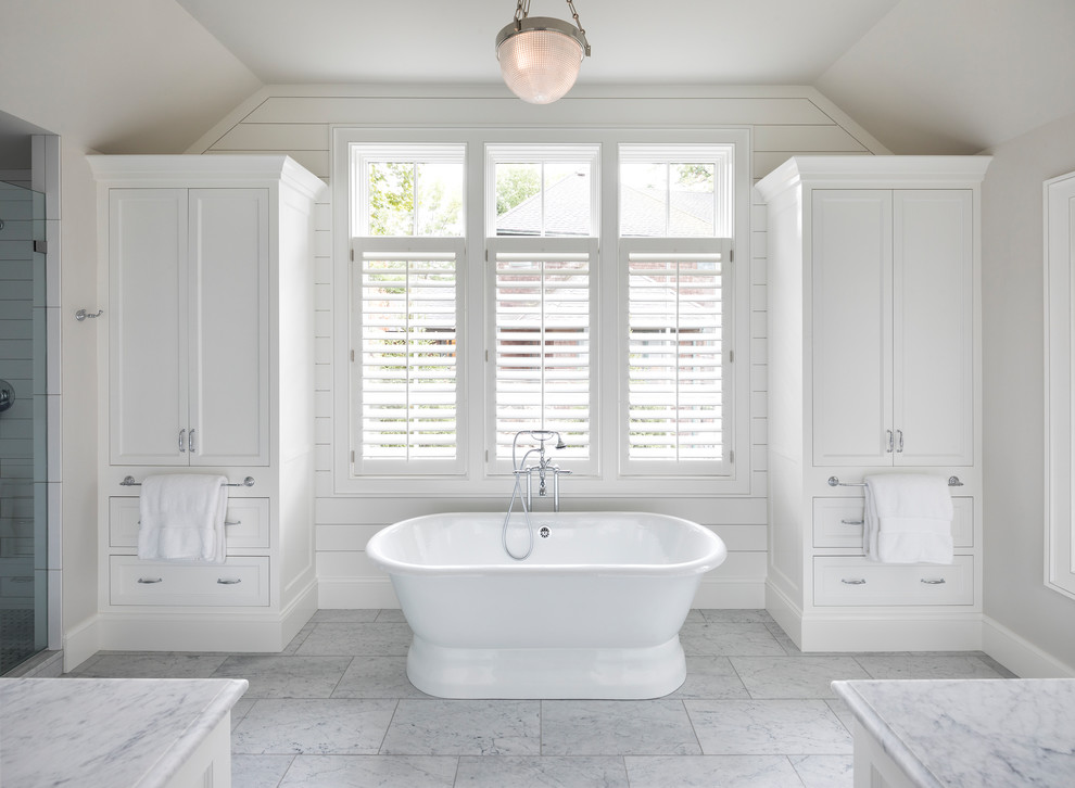 Exemple d'une douche en alcôve bord de mer avec un placard avec porte à panneau encastré, des portes de placard blanches, une baignoire indépendante, un mur gris, un sol blanc et une cabine de douche à porte battante.