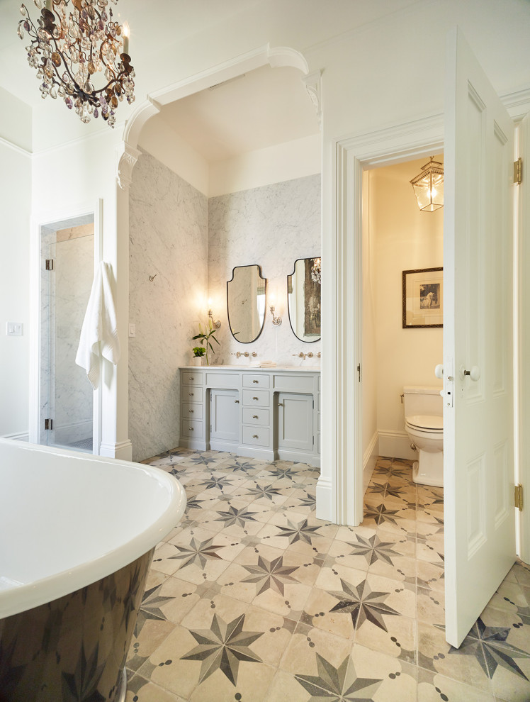 Diseño de cuarto de baño principal, doble y a medida clásico con armarios estilo shaker, puertas de armario grises, bañera exenta, paredes blancas, suelo beige, encimeras blancas y cuarto de baño