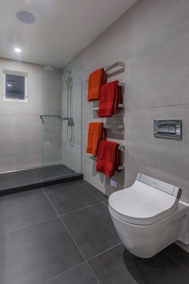 This is an example of a large contemporary shower room bathroom in Auckland with a vessel sink, freestanding cabinets, white cabinets, quartz worktops, a double shower, a wall mounted toilet, grey tiles, porcelain tiles, grey walls and porcelain flooring.