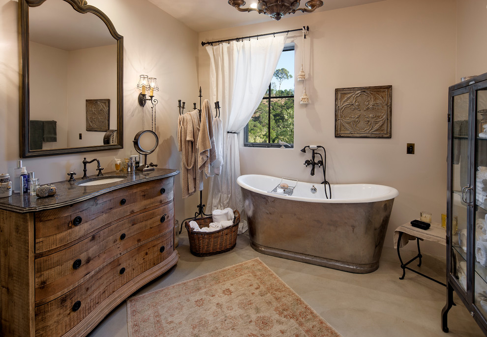 Rural ensuite bathroom in Santa Barbara with a submerged sink, medium wood cabinets, a freestanding bath, beige walls, concrete flooring and flat-panel cabinets.