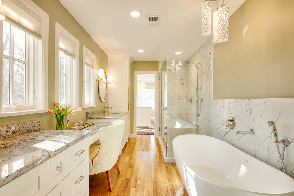This is an example of an expansive traditional ensuite bathroom in Kansas City with shaker cabinets, white cabinets, a freestanding bath, porcelain tiles, green walls, medium hardwood flooring, a submerged sink, granite worktops, a hinged door, a corner shower, white tiles, brown floors and grey worktops.