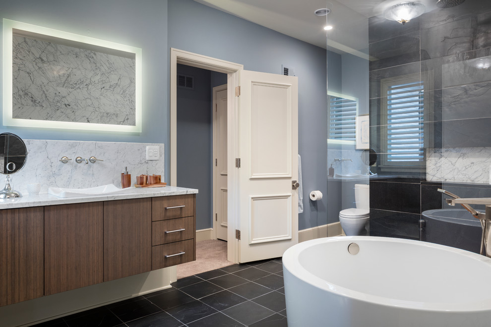 Inredning av ett klassiskt mellanstort badrum, med släta luckor, skåp i mellenmörkt trä, ett japanskt badkar, en öppen dusch, en toalettstol med separat cisternkåpa, svart kakel, stenkakel, blå väggar, skiffergolv, ett fristående handfat och marmorbänkskiva