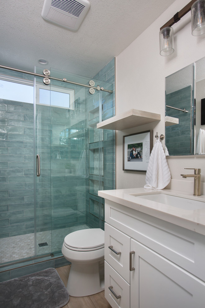 Свежая идея для дизайна: маленькая ванная комната в классическом стиле с фасадами в стиле шейкер, белыми фасадами, накладной ванной, душем над ванной, унитазом-моноблоком, зеленой плиткой, плиткой кабанчик, белыми стенами, полом из ламината, душевой кабиной, врезной раковиной, столешницей из искусственного кварца, коричневым полом, душем с раздвижными дверями, белой столешницей, тумбой под одну раковину и встроенной тумбой для на участке и в саду - отличное фото интерьера