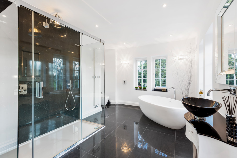 Modern inredning av ett stort en-suite badrum, med möbel-liknande, vita skåp, ett fristående badkar, vit kakel, klinkergolv i porslin, ett konsol handfat, bänkskiva i glas och svart golv