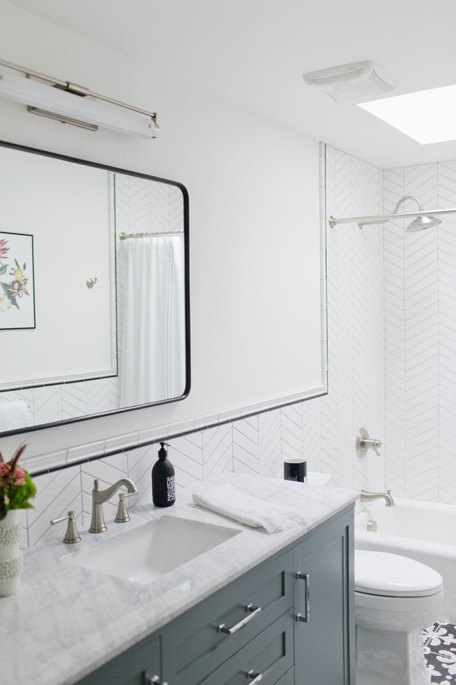 Inspiration för ett mellanstort vintage grå grått badrum med dusch, med möbel-liknande, blå skåp, ett badkar i en alkov, en dusch/badkar-kombination, en toalettstol med hel cisternkåpa, vit kakel, porslinskakel, vita väggar, klinkergolv i porslin, ett undermonterad handfat, marmorbänkskiva, flerfärgat golv och dusch med duschdraperi