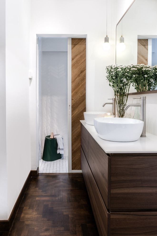 На фото: главная ванная комната в стиле модернизм с плоскими фасадами, темными деревянными фасадами, белой плиткой, белыми стенами, темным паркетным полом, настольной раковиной, коричневым полом и белой столешницей с