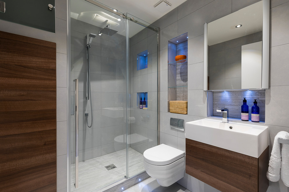 Cette photo montre une petite salle de bain tendance avec un placard à porte plane, des portes de placard marrons, une douche d'angle, WC suspendus, un carrelage gris, un mur gris, un sol gris, une cabine de douche à porte coulissante et un lavabo intégré.