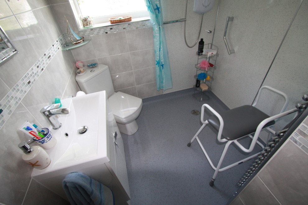 Inredning av ett en-suite badrum, med släta luckor, vita skåp, en öppen dusch, en toalettstol med separat cisternkåpa, grå kakel, keramikplattor, grå väggar och linoleumgolv