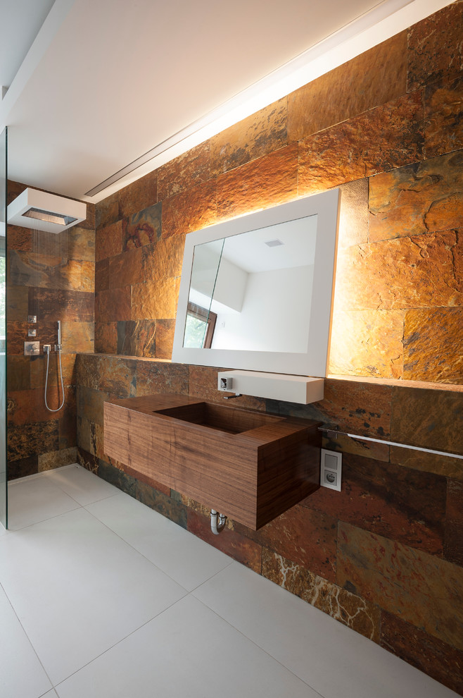 На фото: ванная комната в современном стиле с плоскими фасадами, темными деревянными фасадами, столешницей из дерева, открытым душем, коричневой плиткой, каменной плиткой и открытым душем